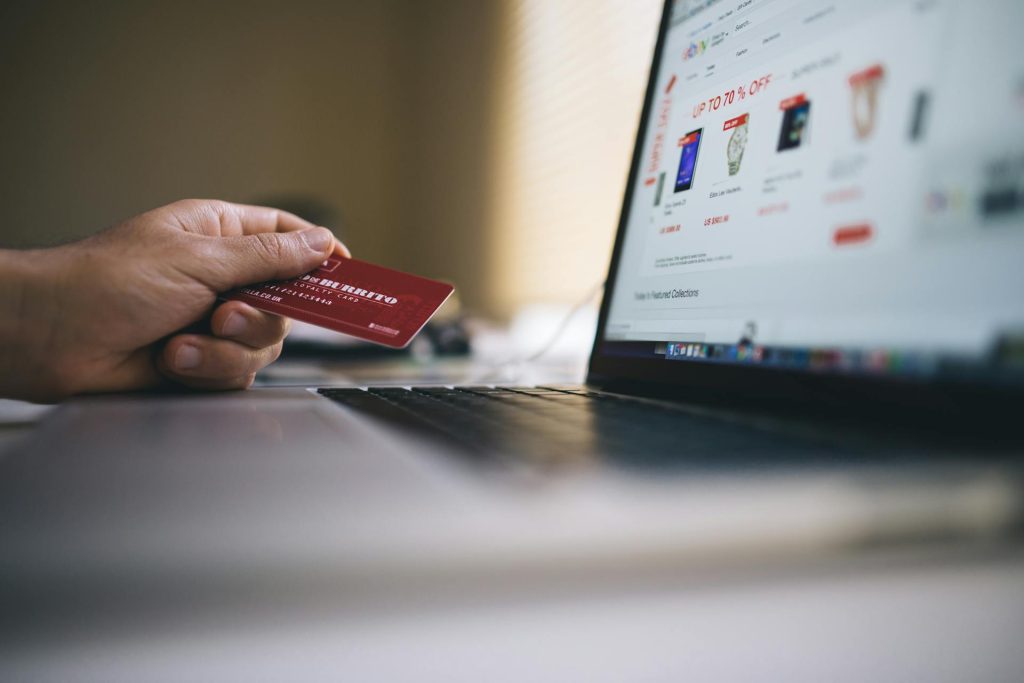 Person holding a credit card while browsing products on an online shopping website on a laptop